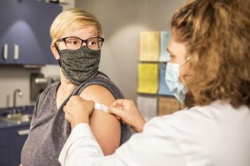 A woman wearing a face mask has a plaster applied to her arm by a nurse.