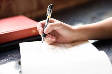 A close up of someone holding a pen and writing in a notebook