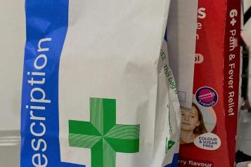 A white and blue paper bag with a green cross on it, and the word 'prescriptions' in white text.