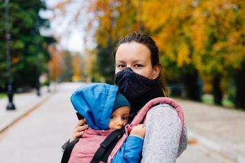 Mum wearing a mask carrying a baby in a sling 