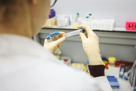 Close up of a person wearing a white lab coat holding a test tube 