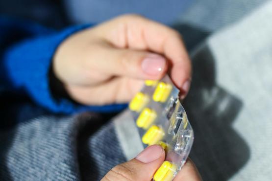 A close up of hands holding a blister pack of yellow pills