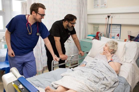 Two male doctors talking to a woman in a hospital bed