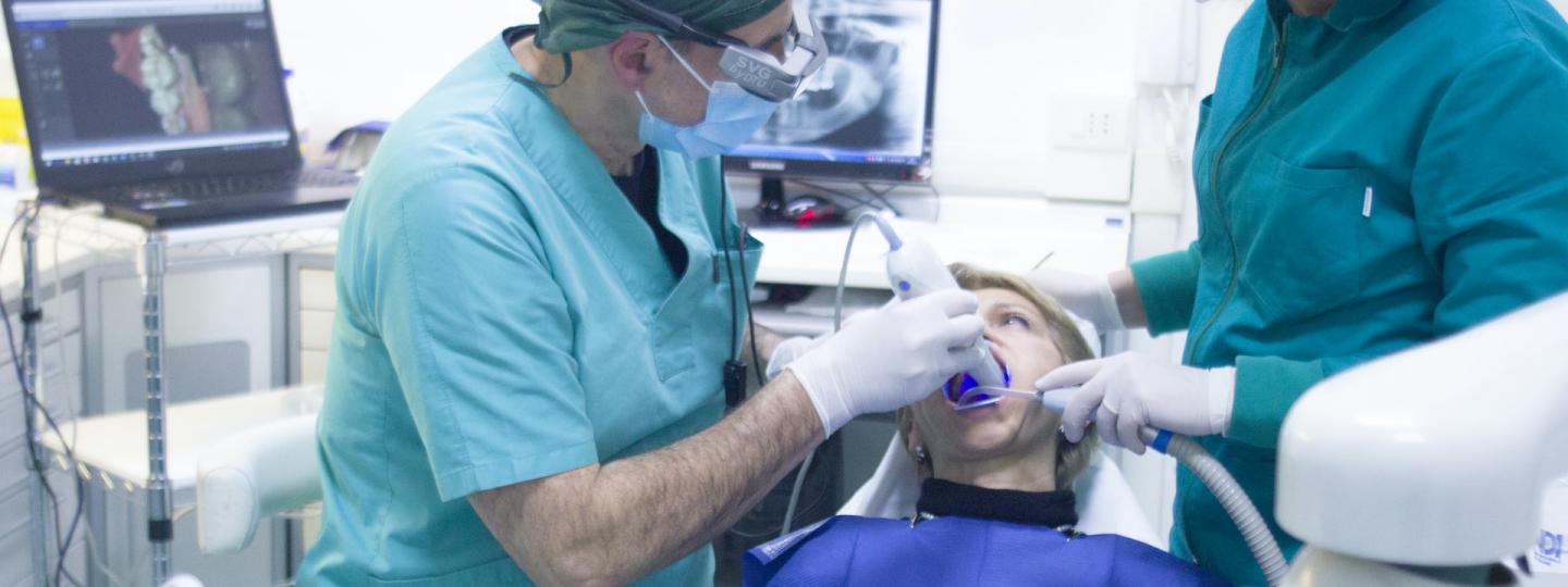 Patient in a dentist's chair with a dentist wearing a mask and turquoise scrubs