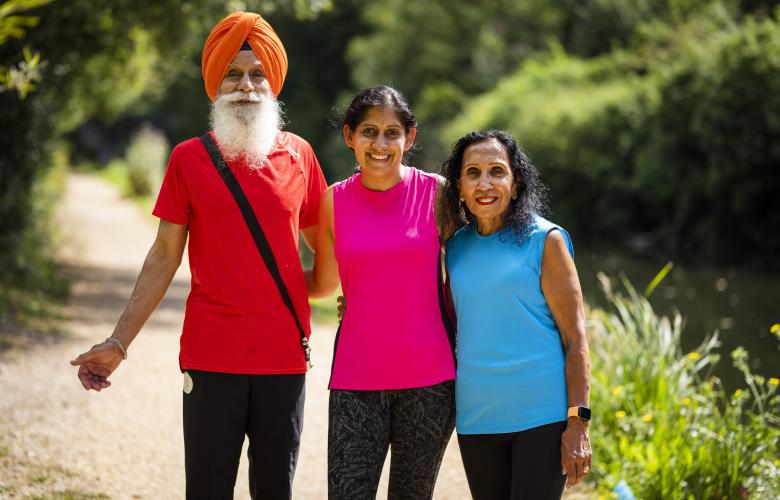 A man and two women stand together surrounded by greenery. They are all wearing bright colours and the sun is shining.