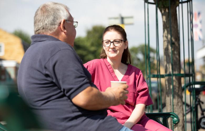 A man wearing a blue t shirt is sitting next to a doctor in red scrubs