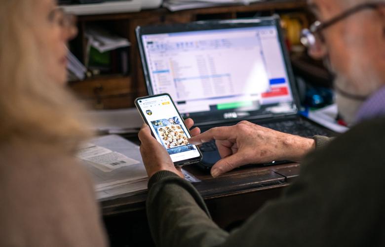 Close up of a man wearing glasses looking at a laptop and phone screen