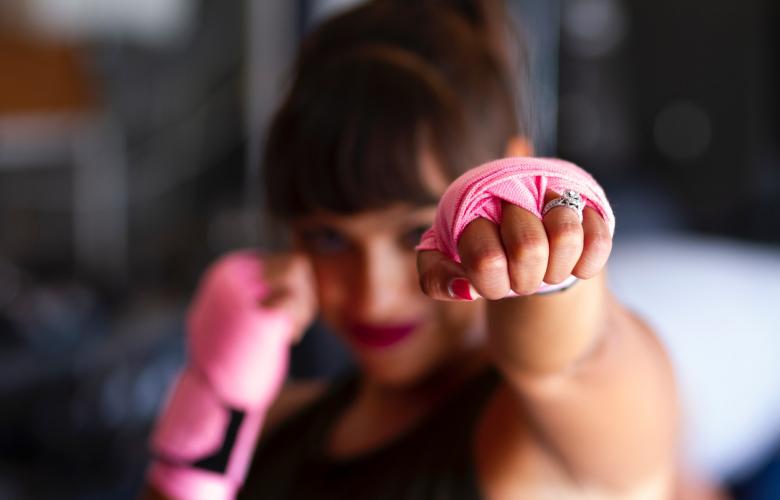 A young woman wearing pink gloves punches towards the camera 