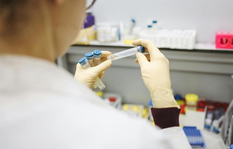 Close up of a person wearing a white lab coat holding a test tube