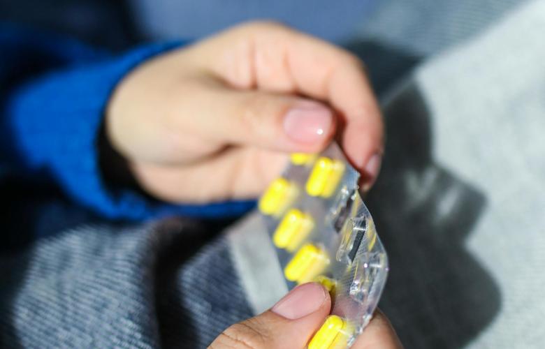 A close up of hands holding a blister pack of yellow pills
