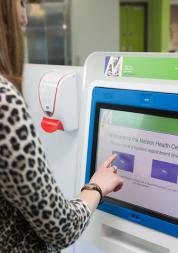A woman wearing a leopard print top standing next to a GP surgery self check in station